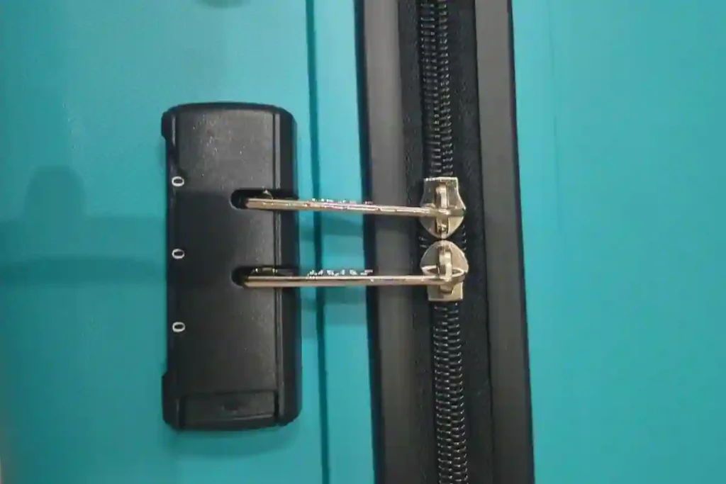 Close-up of the built-in number lock and zipper pulls on a blue hard-shell trolley bag, showing the integrated locking system for added travel security